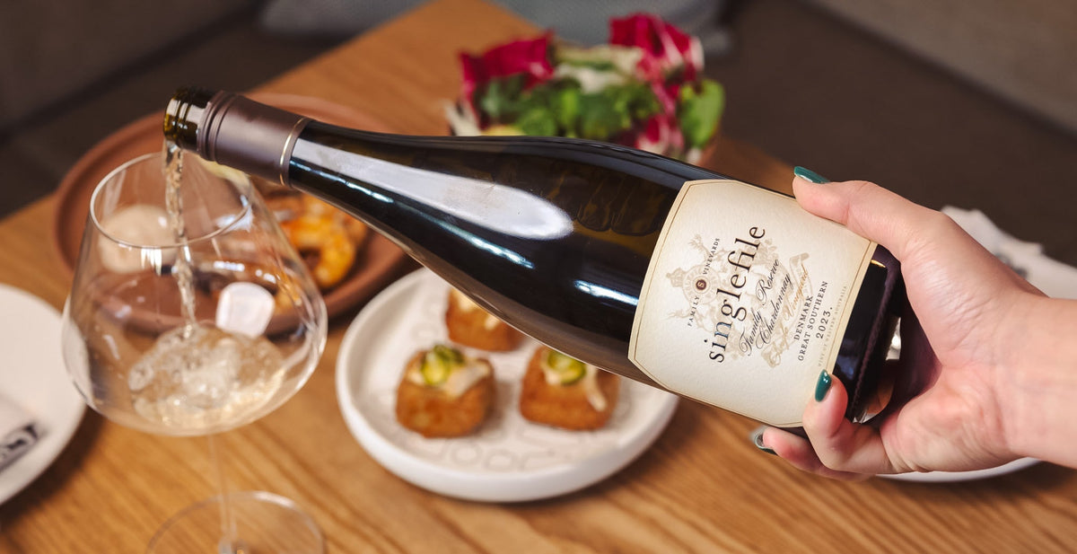 A bottle of Singlefile white wine held at a restaurant table set with canapes and glasses
