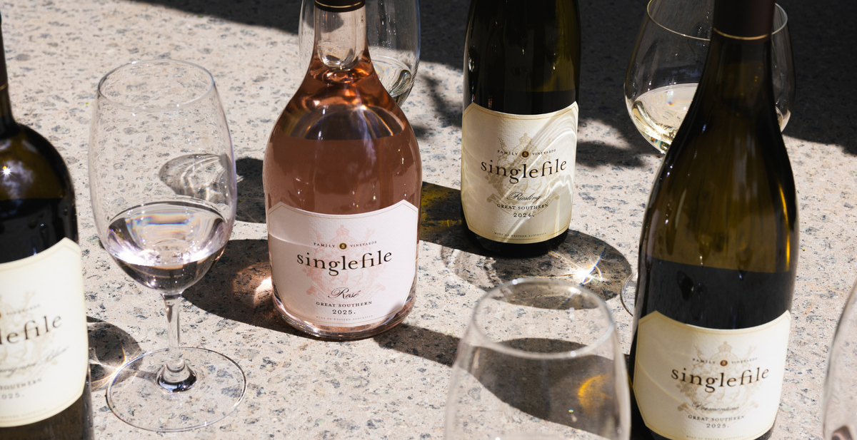Singlefile rose and white bottles with glasses on a sunlit table set for a barbecue