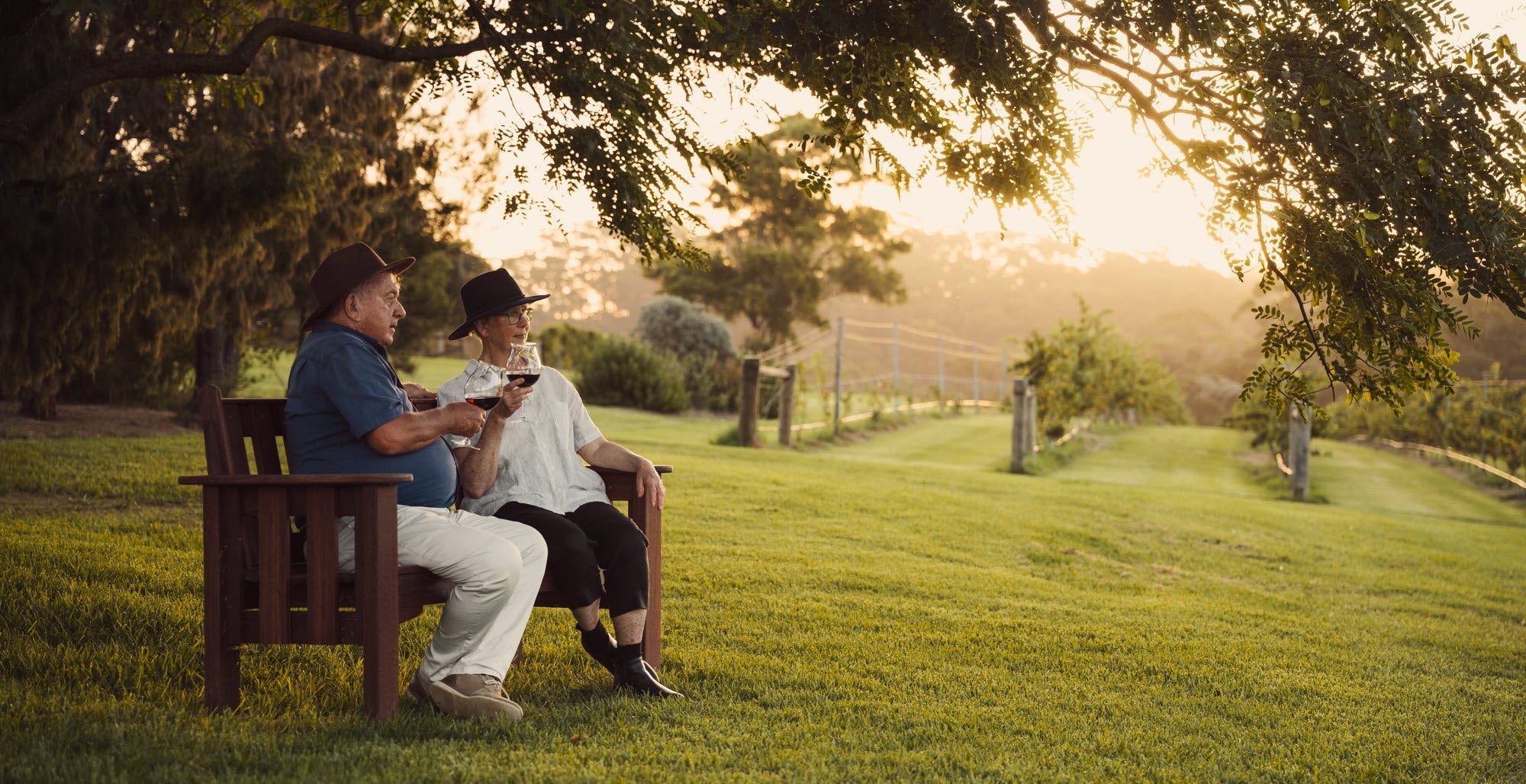 Phil and Viv sitting on a bench in the vineyard enjoying a glass of Pinot Noir