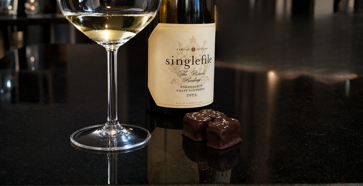 A glass of wine with a Singlefile Small Batch bottle and a dark chocolate truffle