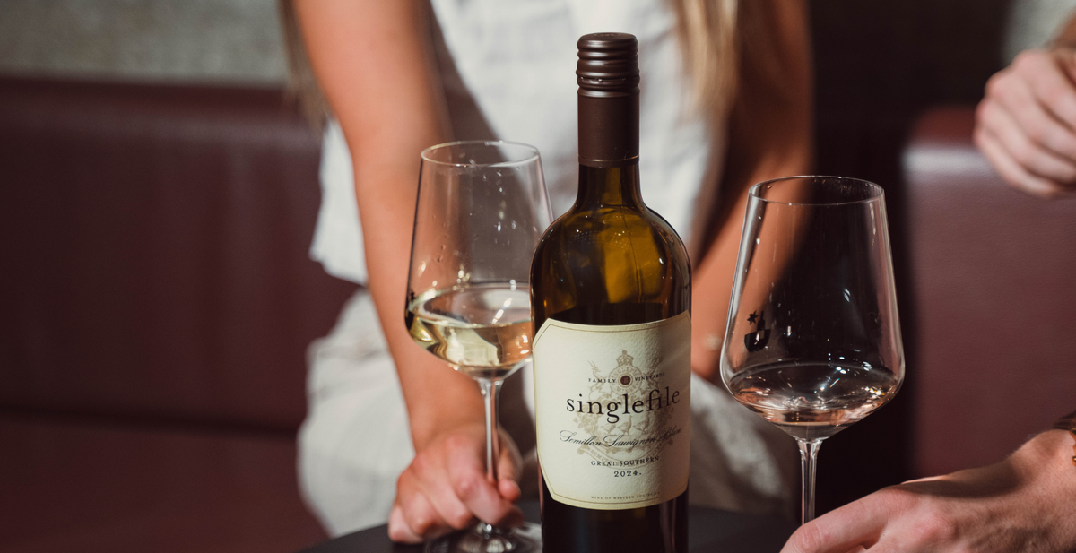 Friends holding glasses of white wine around a Singlefile bottle on a table