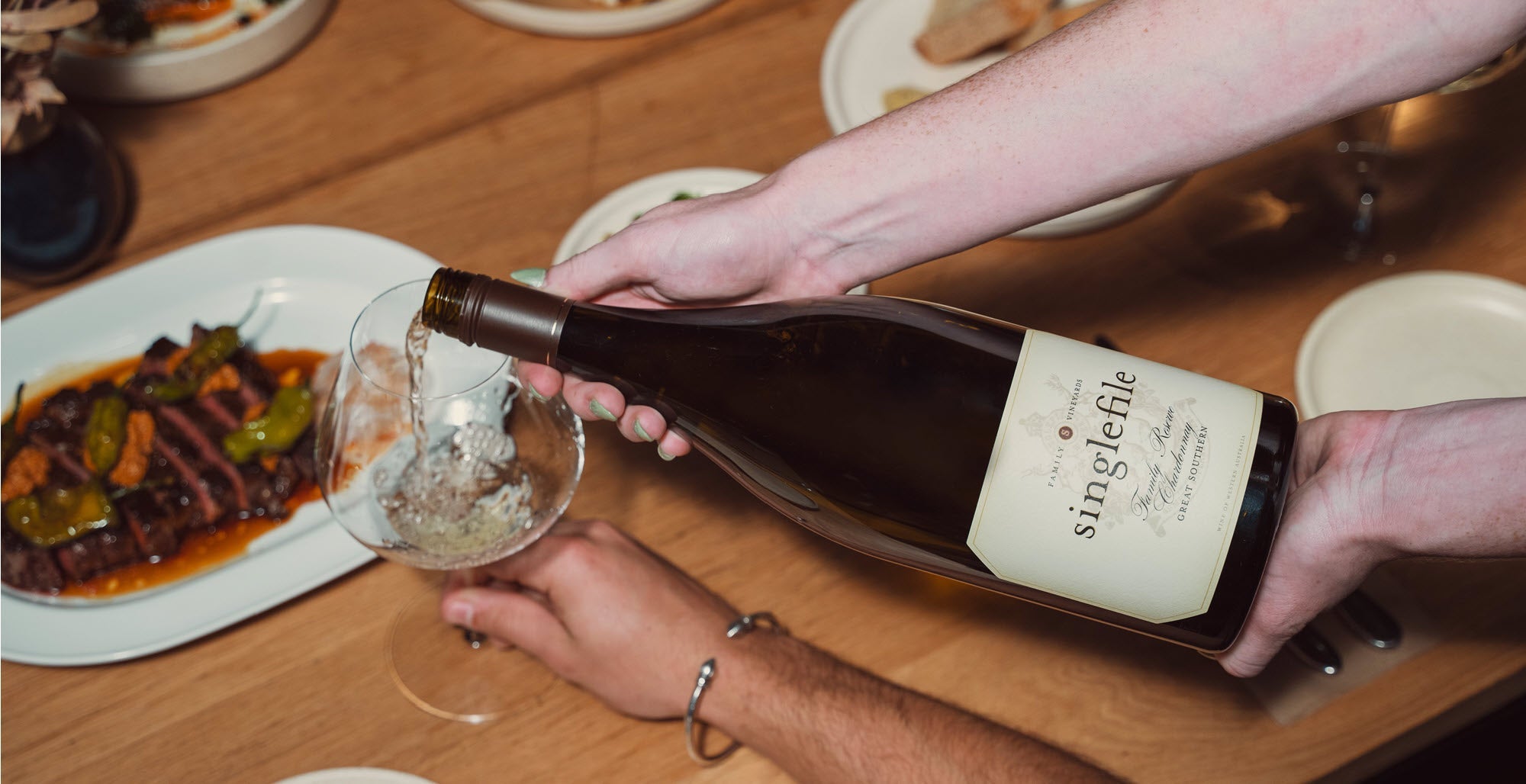 A glass of white wine being poured in to a glass on a dinner table