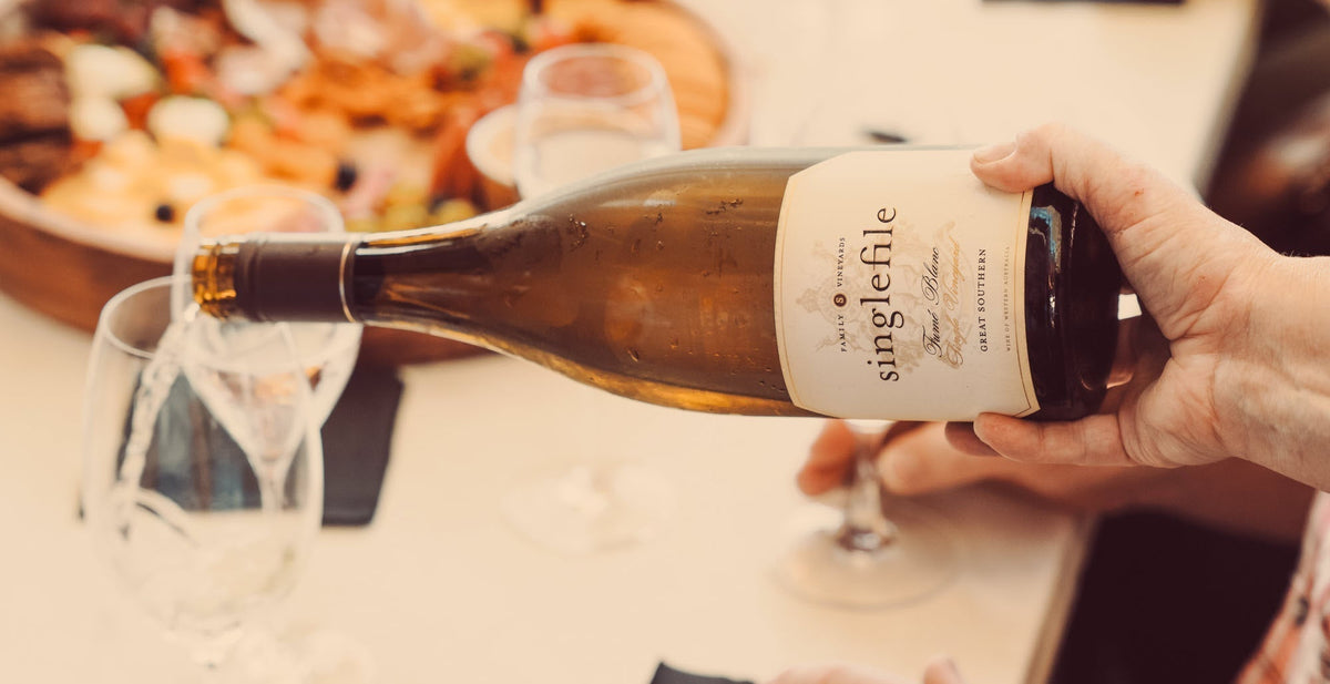 Pouring Singlefile fume blanc into glasses beside a grazing board of shared food