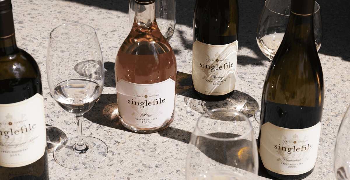 Singlefile white and rose bottles with glasses on a pale stone bench in winter light