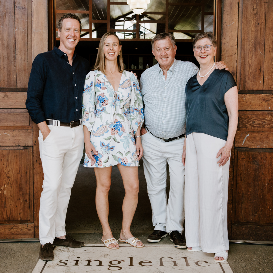 Four people posing together in front of a wooden door with 'singlefile' rug.