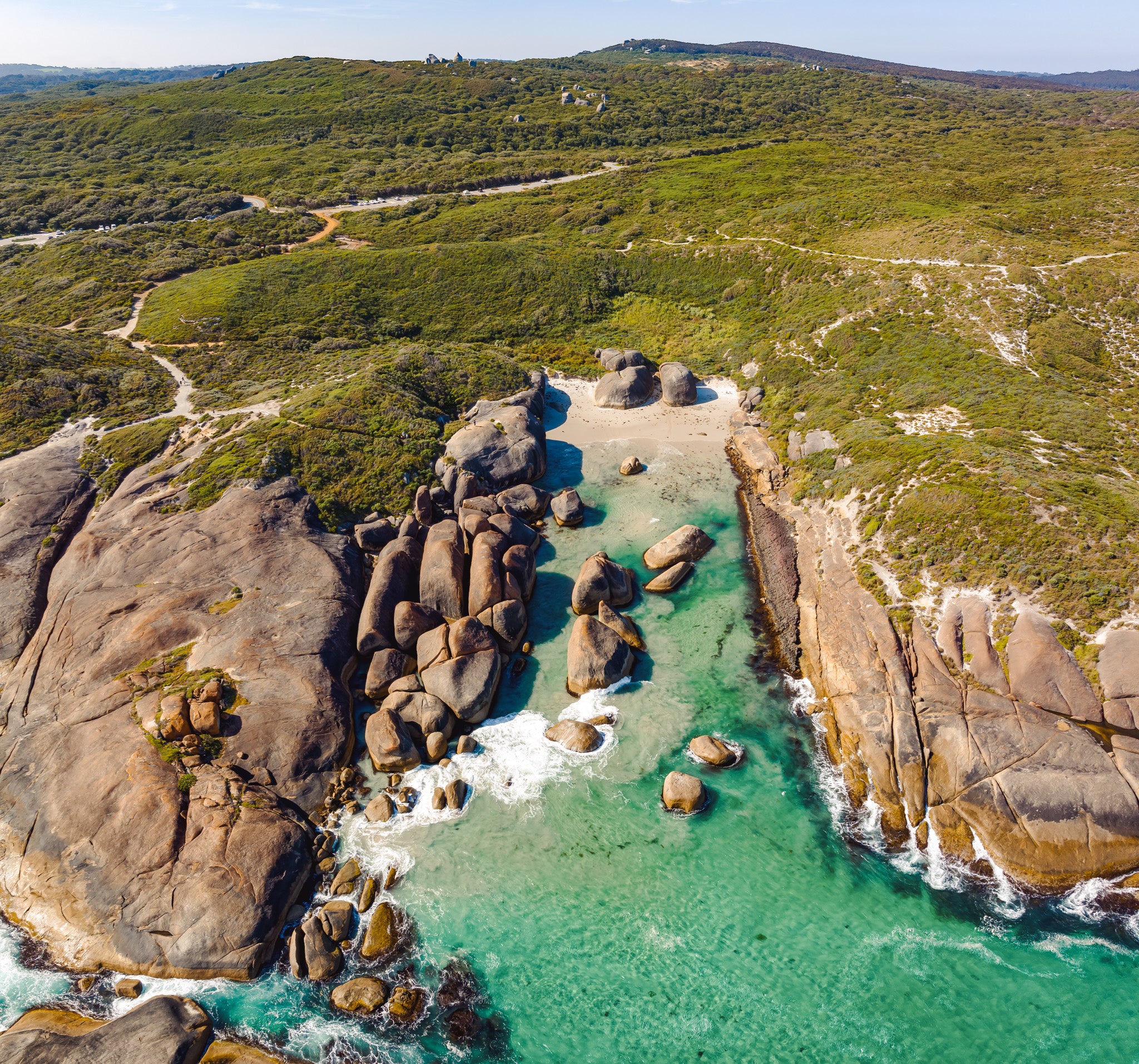 Aerial view of rocky coastline with clear turquoise water and green landscape.