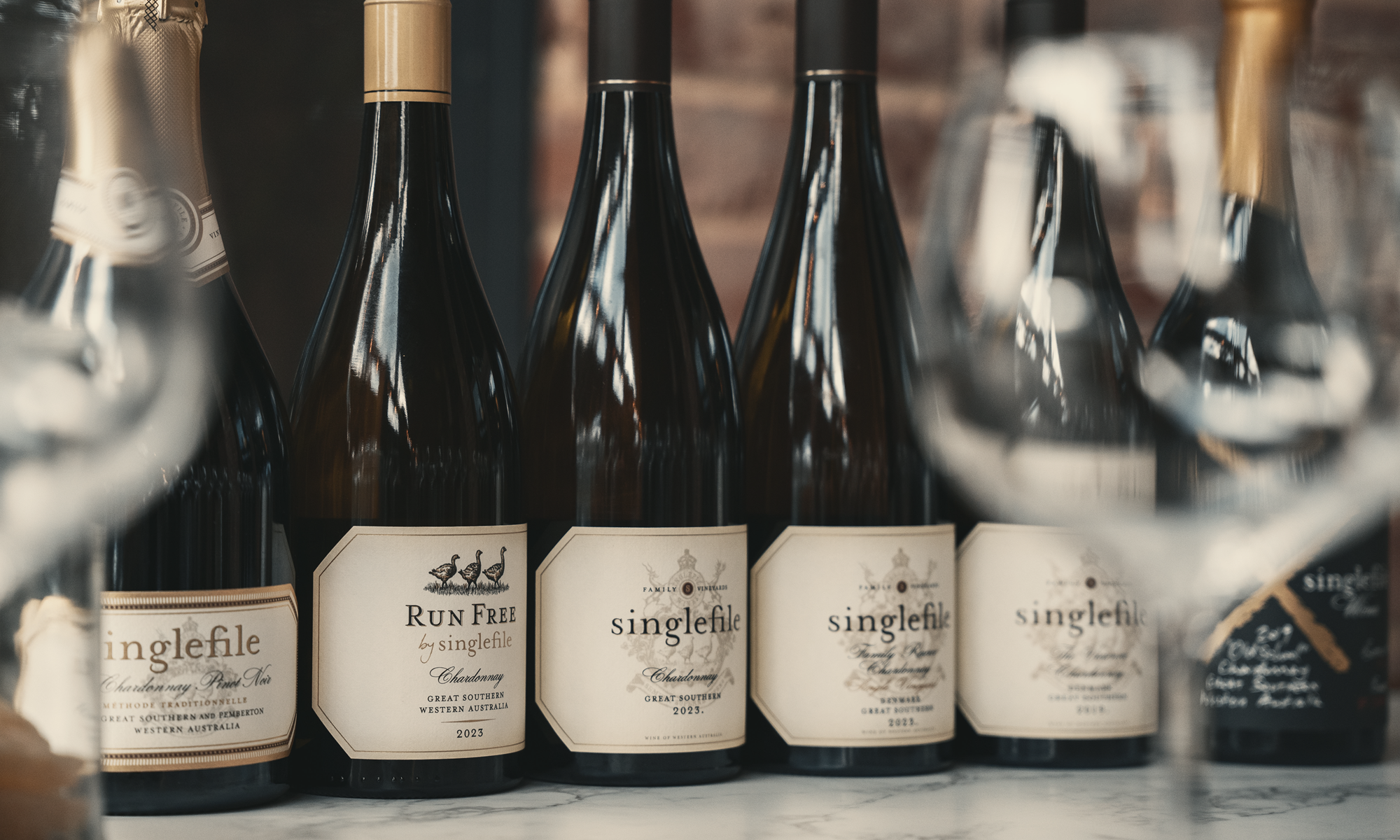 Row of wine bottles with 'singlefile' labels on a wooden surface.