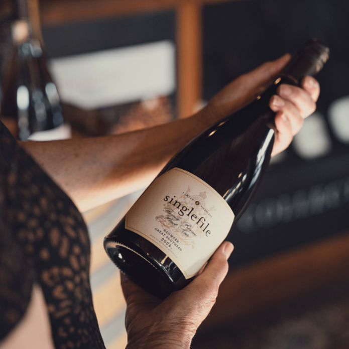 Person holding a bottle of 'singlefile' wine with a blurred background