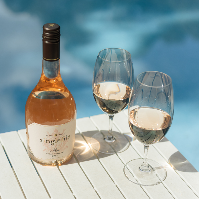 Bottle of Singlefile Rosé wine with two glasses on a wooden surface by a pool.
