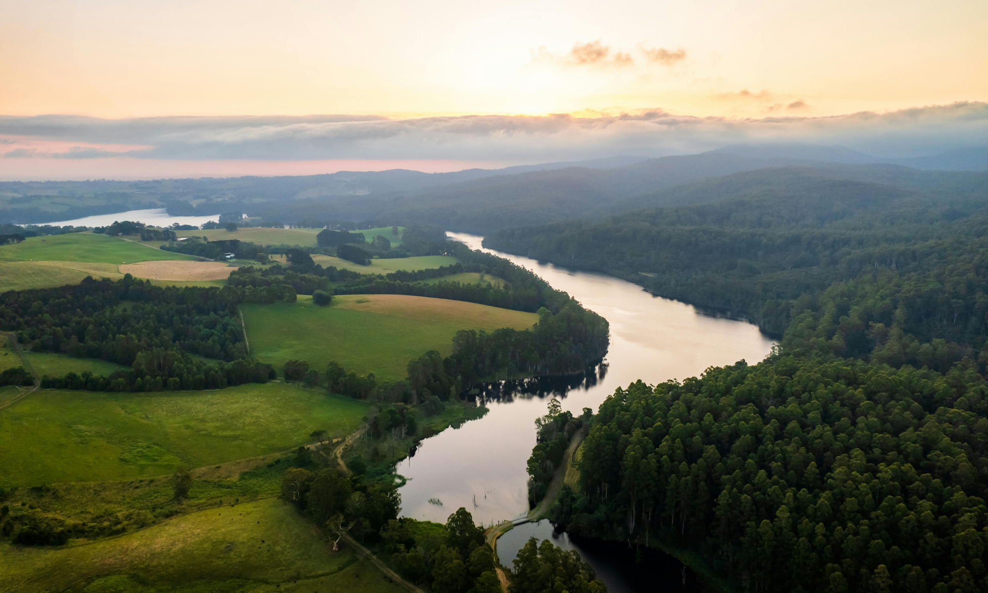 River winding through a landscape with green fields and trees at sunset.