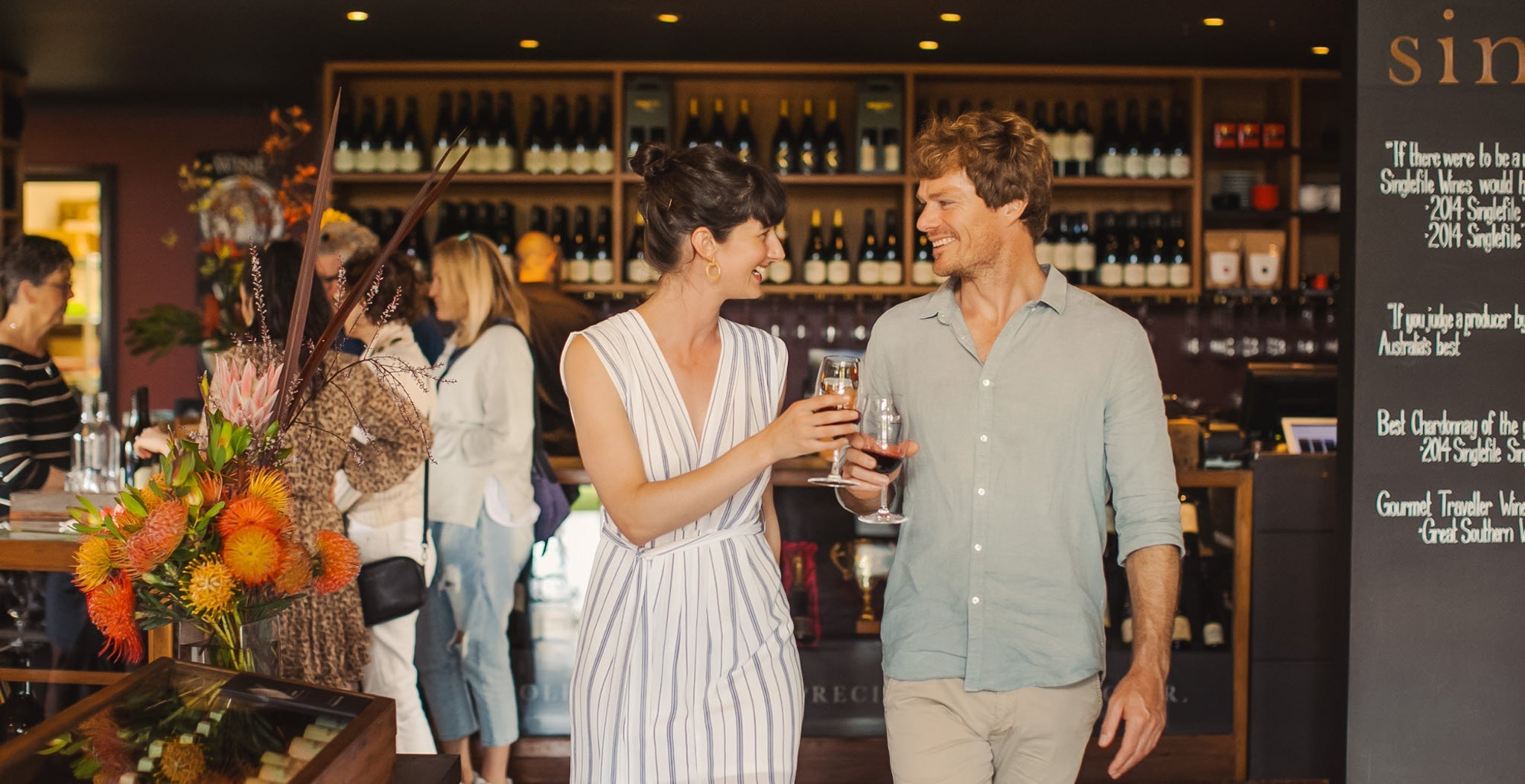 A couple smiling and walking through the cellar door with glasses of wine