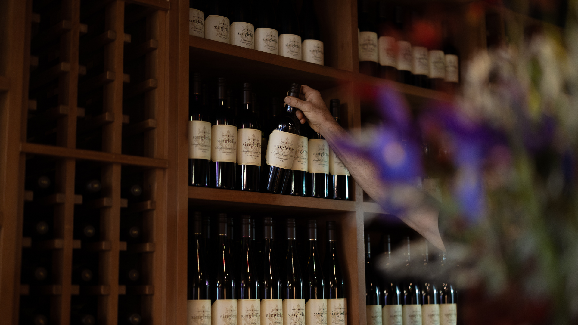 Person selecting a bottle from a wine rack in a dimly lit room