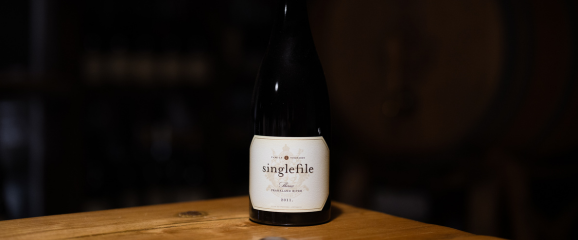 Wine bottle labeled 'singlefile' on a wooden surface with a dark background