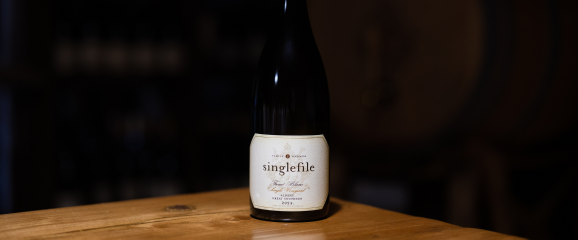 Wine bottle labeled 'singlefile' on a wooden surface with a dark background