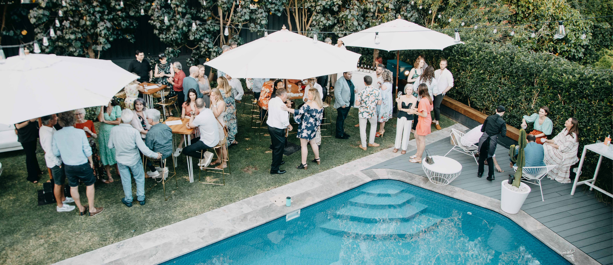 People socialising by a pool with white umbrellas