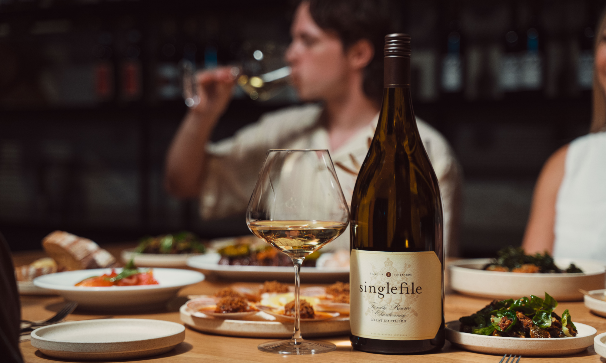 Bottle of Singlefile wine with a glass on a table with people in the background