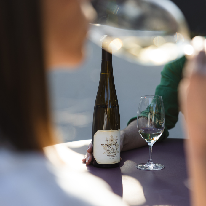 Wine bottle labeled 'singlefile' with a glass of wine on a table, blurred background