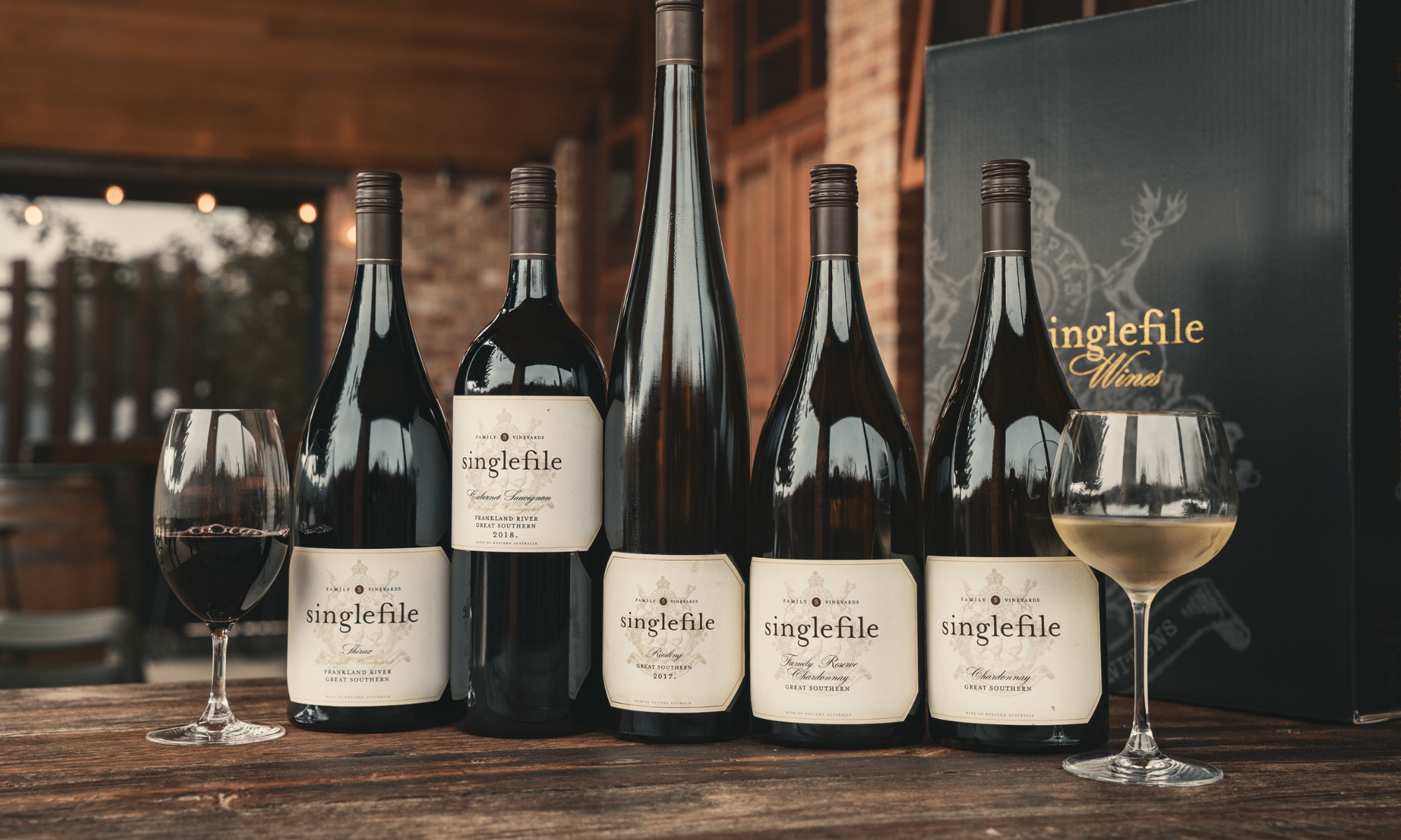 Collection of Singlefile wine bottles and glasses on a wooden table with a blurred background.