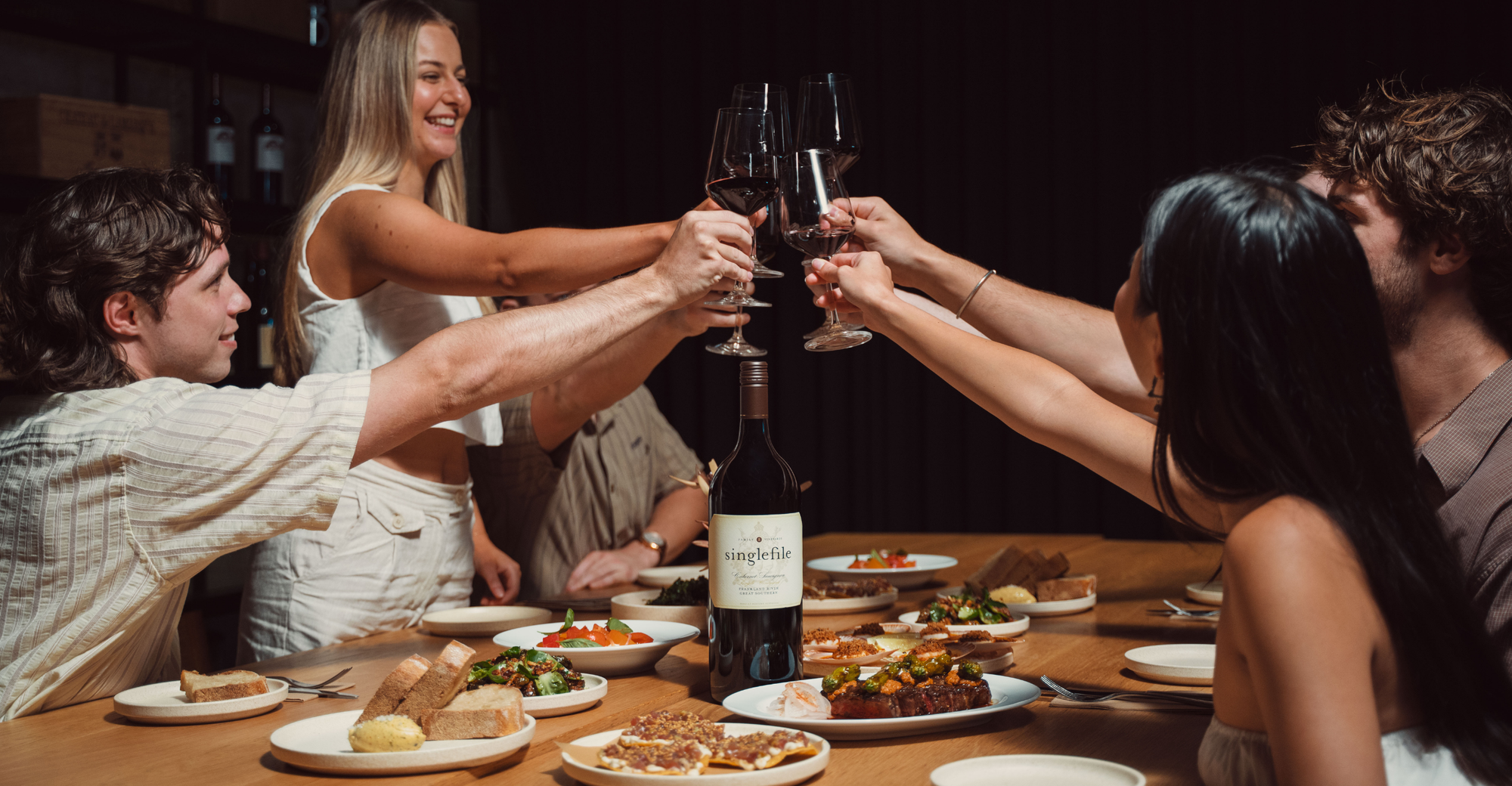 Group of people toasting with wine glasses at a dinner table.