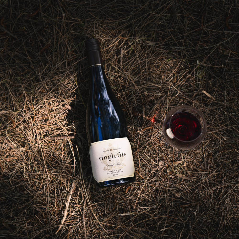 Wine bottle labeled 'singlefile' on straw with a glass of red wine beside it.