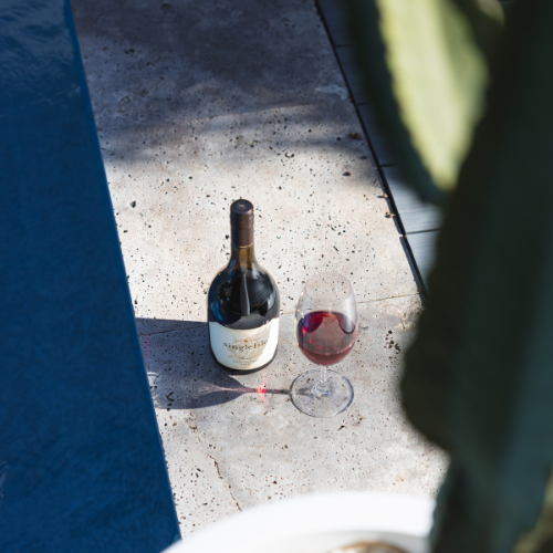 Bottle of wine and red glass next to a pool