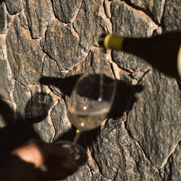 Wine being poured into a glass against a stone wall