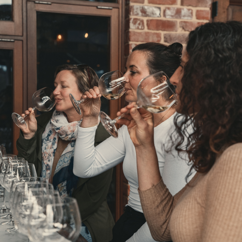 Three women at a table with wine glasses in a social setting.