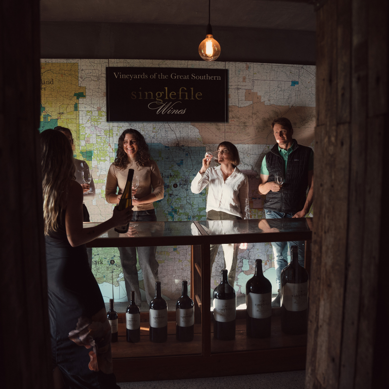 People tasting wine in a cellar with 'singlefile Wines' sign on the wall.