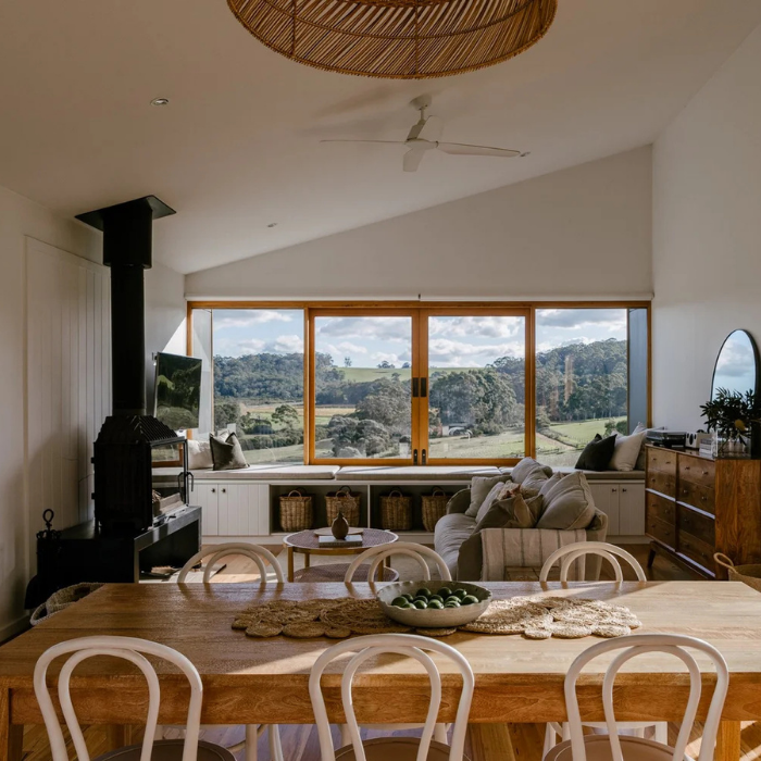 Modern living room with large windows, wooden dining table, and chairs.